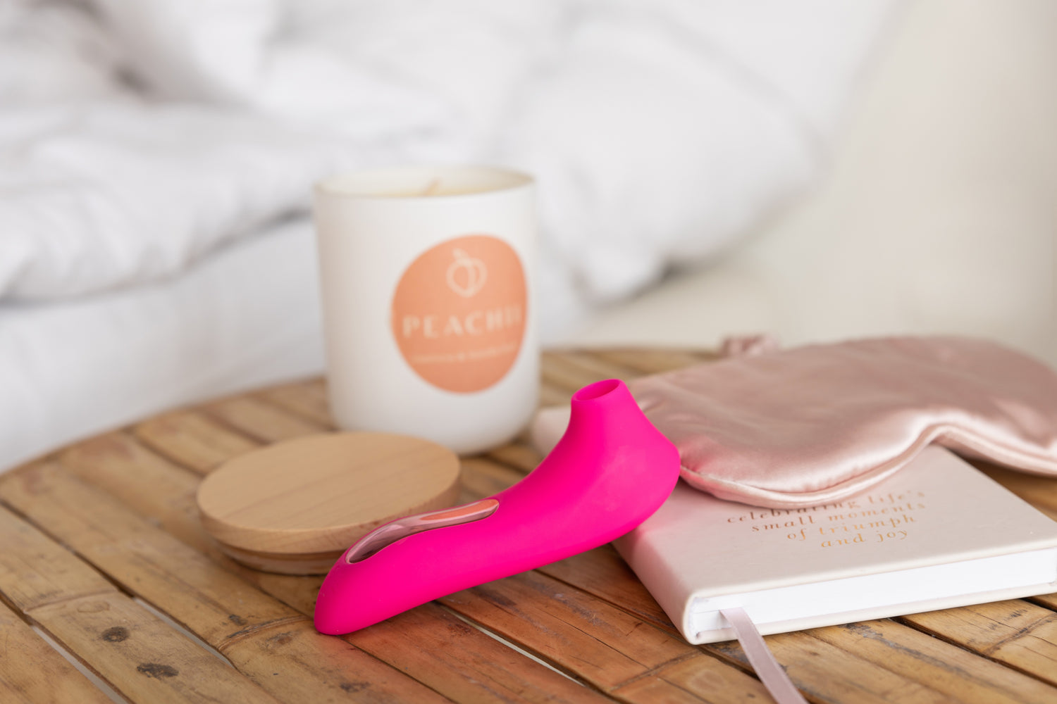 A cozy morning scene with Peachii's 'Little Pink' resting on a wooden table alongside a Peachii scented candle, a pink sleep mask, and a journal. This serene setup symbolizes relaxation and self-care. Peachii's commitment to sustainability is evident through their sex toy recycling program, ensuring that products like 'Little Pink' contribute to a greener, more eco-friendly world.