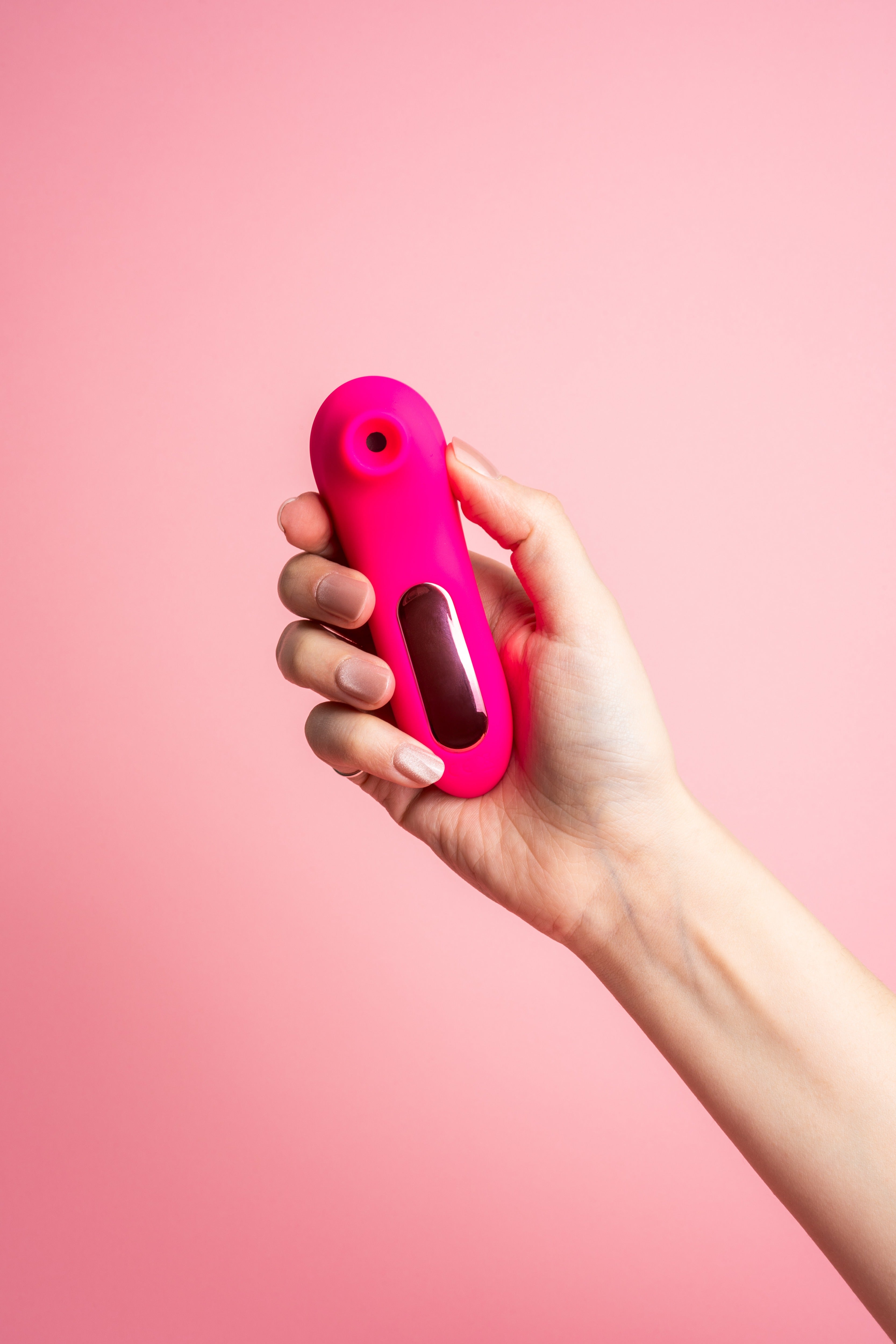 A hand is elegantly poised against a pink backdrop, holding the "Little Pink" device by Peachii, an emblem of personal well-being and self-care.