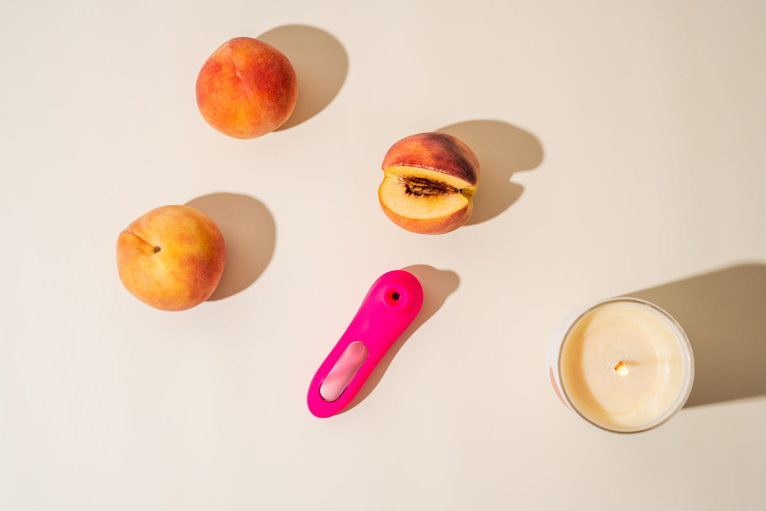 On a sunlit surface, Peachii's "Little Pink" device lies elegantly beside freshly cut peaches and a gently burning candle, setting a scene of tranquil self-care and sensory enjoyment.